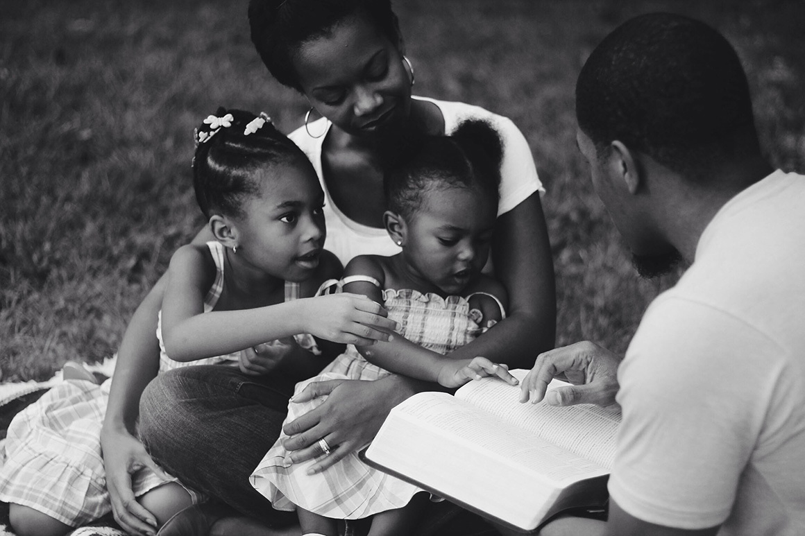 Stock family looking at bible together bw